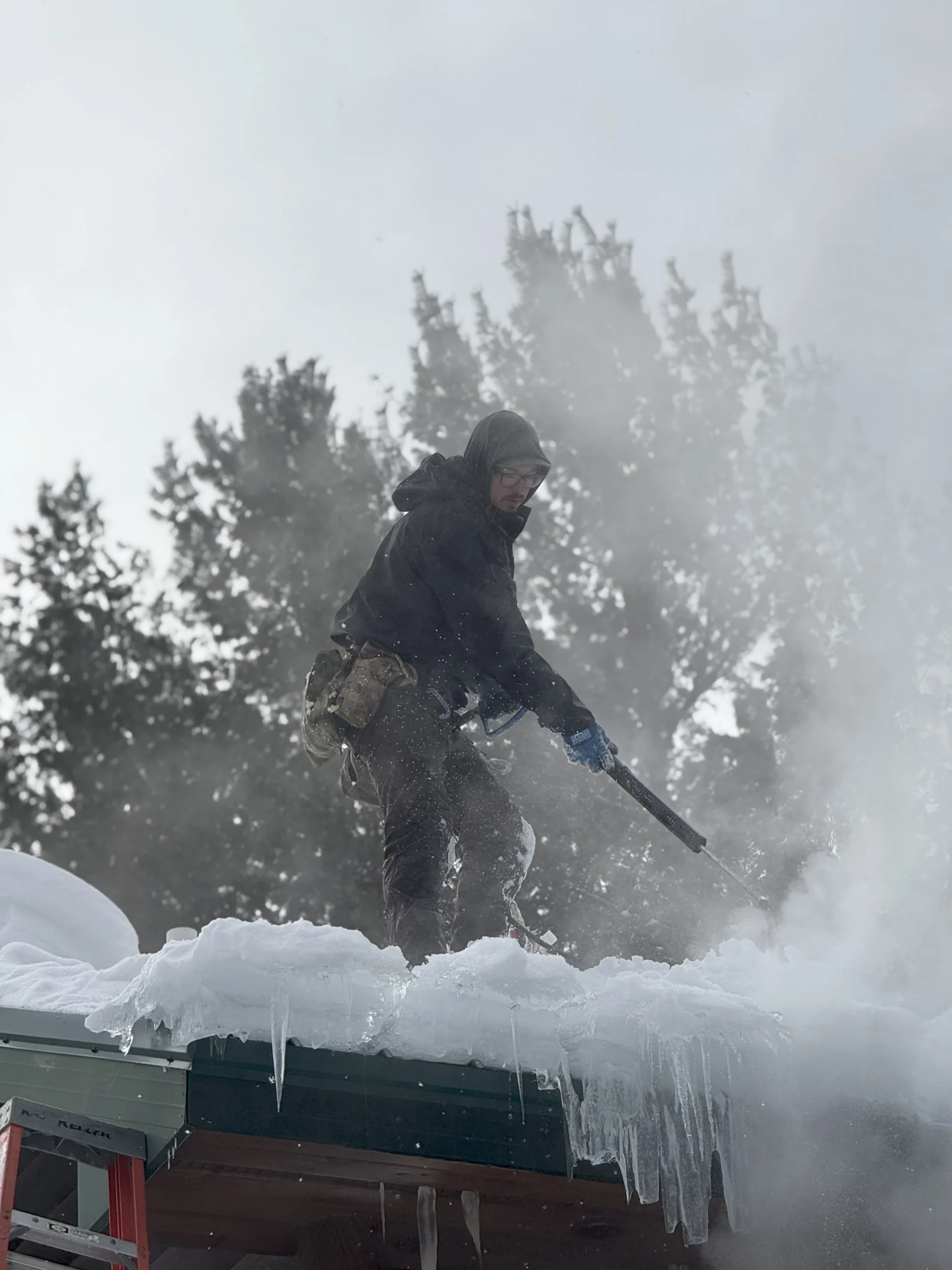 Technician removing heavy snow and ice dams from a roof in Northern Michigan.